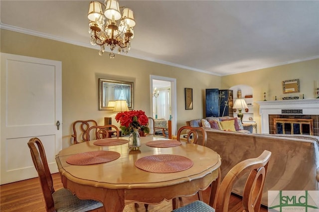 dining space featuring an inviting chandelier, a tiled fireplace, crown molding, and wood finished floors