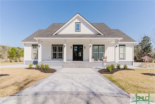 modern inspired farmhouse featuring covered porch, a shingled roof, french doors, a front lawn, and board and batten siding