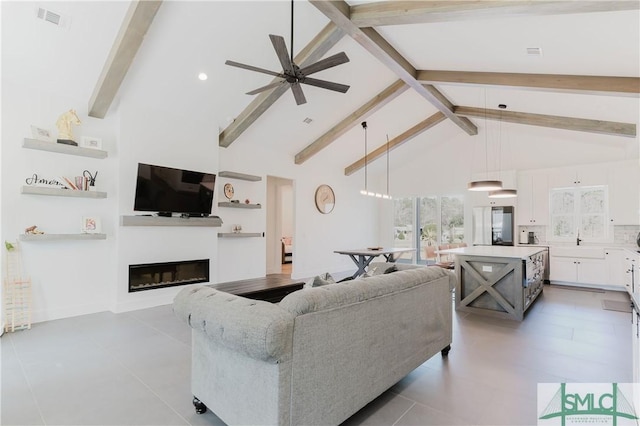 living room featuring visible vents, a ceiling fan, a glass covered fireplace, high vaulted ceiling, and beamed ceiling