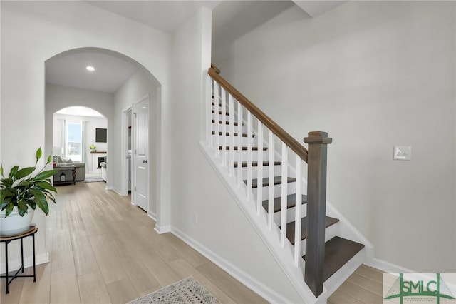 stairway featuring arched walkways, recessed lighting, baseboards, and wood finished floors