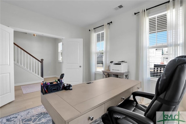 office area with a healthy amount of sunlight, light wood-style flooring, visible vents, and baseboards