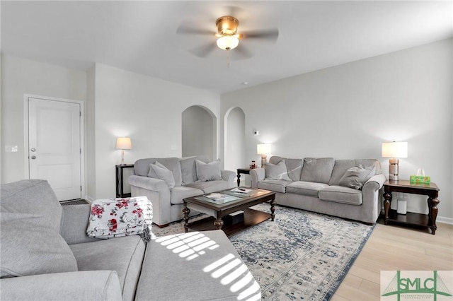 living room featuring arched walkways, ceiling fan, wood finished floors, and baseboards