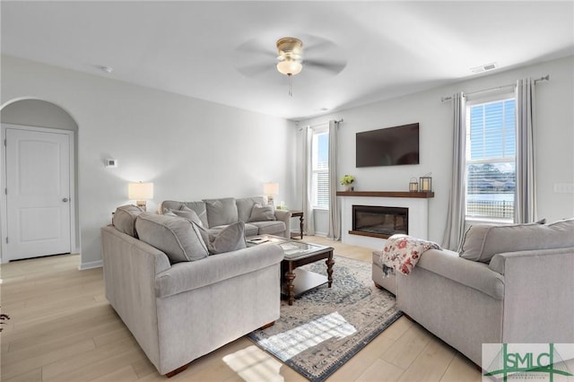 living room with arched walkways, a glass covered fireplace, a wealth of natural light, and light wood-style floors