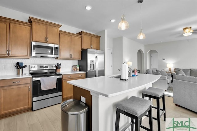 kitchen with arched walkways, a sink, open floor plan, appliances with stainless steel finishes, and brown cabinetry