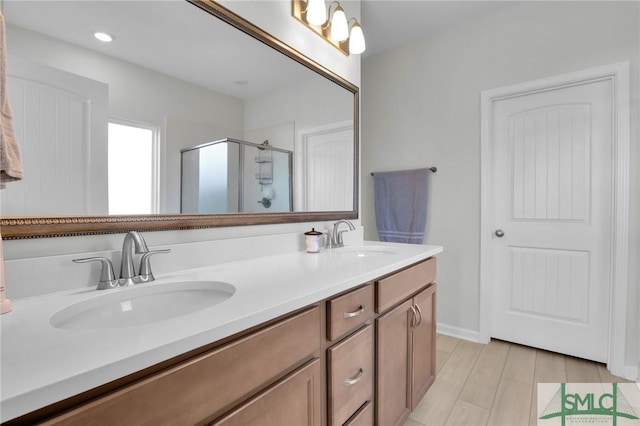 full bathroom featuring double vanity, a shower stall, a sink, and wood finished floors