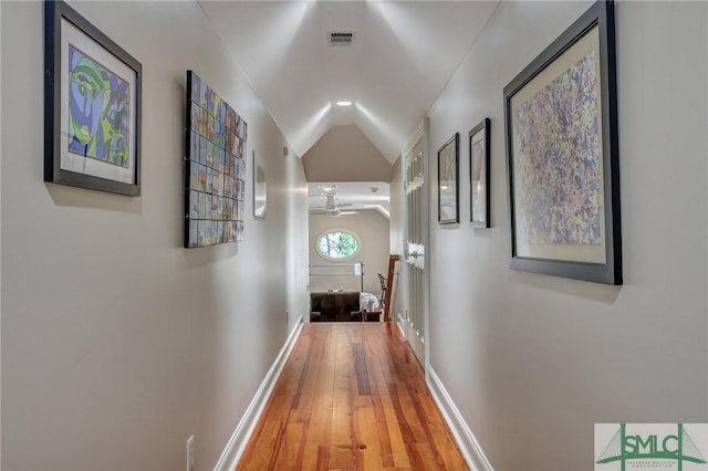 hall with baseboards, visible vents, vaulted ceiling, and wood finished floors