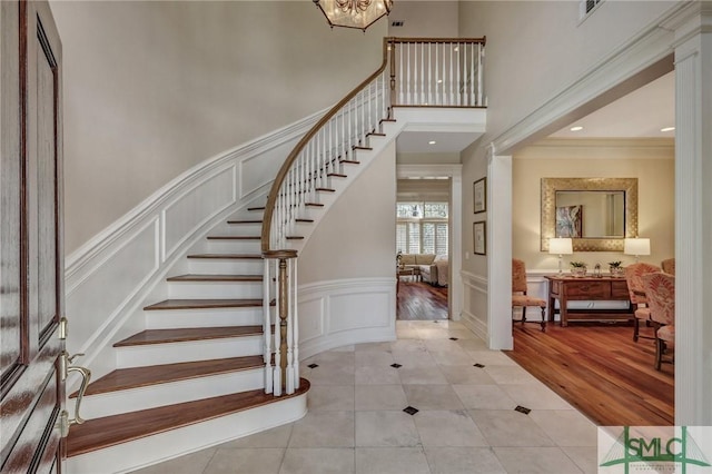 foyer featuring light tile patterned floors, a decorative wall, a high ceiling, stairs, and ornamental molding