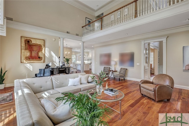 living room with wood finished floors, a towering ceiling, baseboards, decorative columns, and crown molding