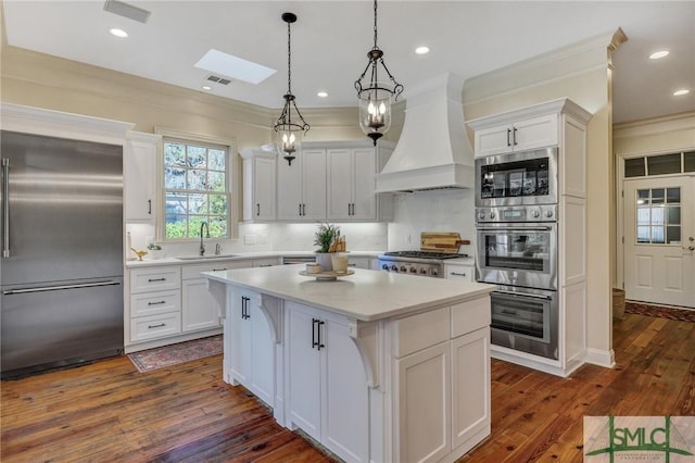 kitchen featuring a center island, built in appliances, custom exhaust hood, light countertops, and a sink