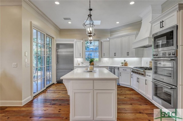 kitchen with crown molding, dark wood-type flooring, white cabinetry, built in appliances, and premium range hood