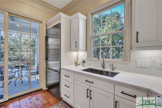 kitchen with hardwood / wood-style floors, stainless steel built in fridge, light countertops, crown molding, and a sink