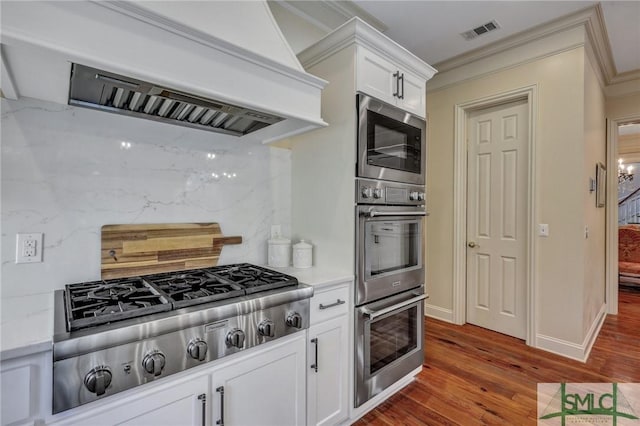 kitchen with premium range hood, visible vents, white cabinets, ornamental molding, and appliances with stainless steel finishes