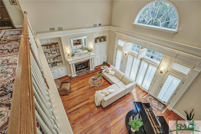 living room with built in features, visible vents, a high ceiling, a premium fireplace, and wood finished floors