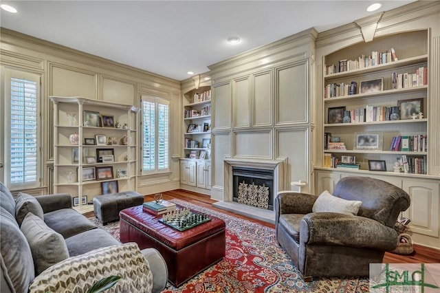 living area featuring ornamental molding, built in shelves, a fireplace, and wood finished floors