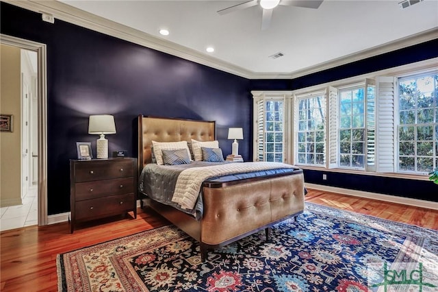 bedroom with crown molding, visible vents, ceiling fan, wood finished floors, and baseboards