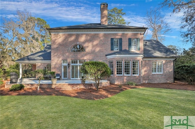 rear view of house with a yard, brick siding, a chimney, and a patio