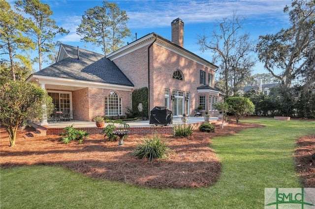 back of house featuring a patio area, a lawn, a chimney, and brick siding