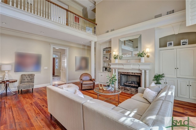 living room with built in shelves, a high end fireplace, baseboards, and wood finished floors