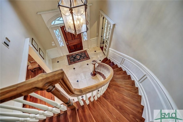 entrance foyer with a notable chandelier, a wainscoted wall, a decorative wall, a high ceiling, and stairway