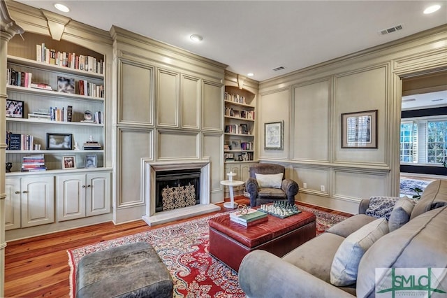 living room with a fireplace with raised hearth, a decorative wall, visible vents, built in features, and light wood finished floors