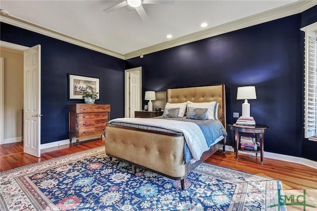 bedroom with ornamental molding, an accent wall, baseboards, and wood finished floors