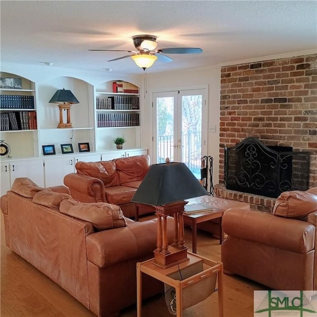 living area with a textured ceiling, built in shelves, wood finished floors, french doors, and a brick fireplace