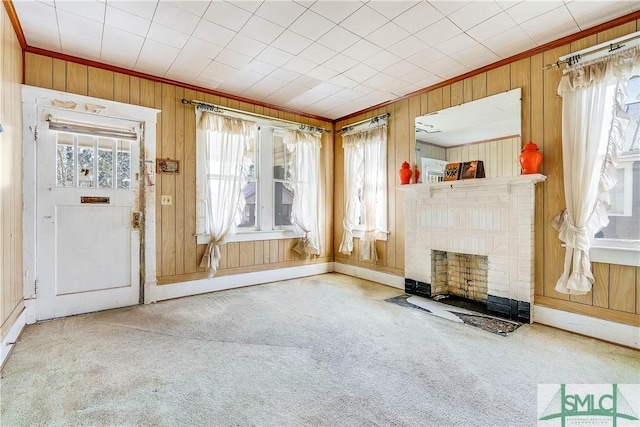 unfurnished living room with carpet floors, wood walls, a fireplace, and crown molding