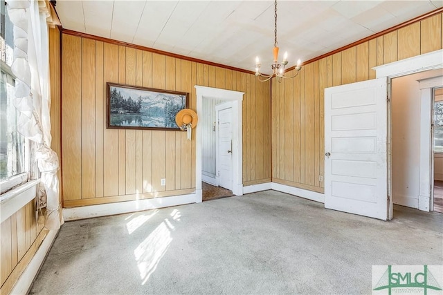 interior space with wood walls, carpet, ornamental molding, and a notable chandelier