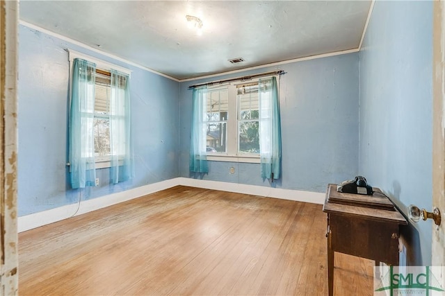 empty room with baseboards, wood finished floors, visible vents, and crown molding