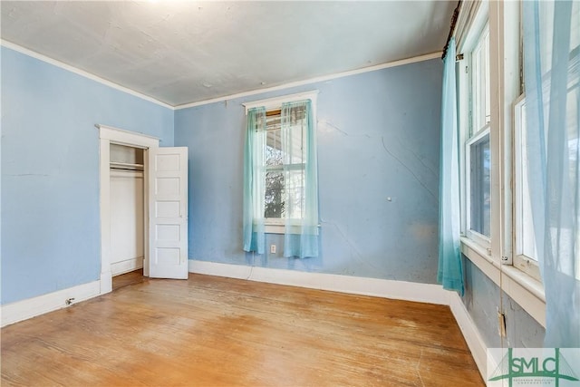 unfurnished bedroom featuring a closet, crown molding, baseboards, and wood finished floors