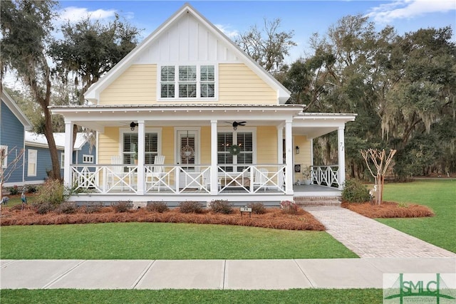 view of front of home with board and batten siding, covered porch, a front lawn, and a ceiling fan