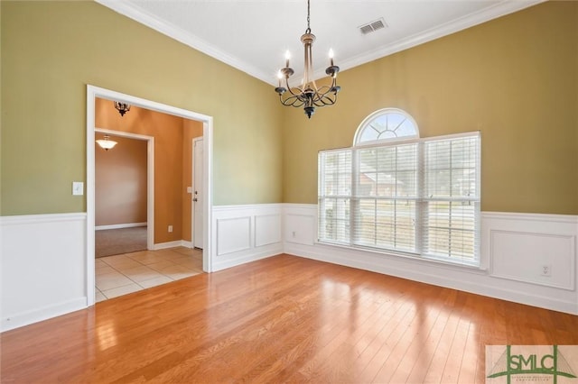 empty room with a chandelier, wood finished floors, visible vents, ornamental molding, and wainscoting