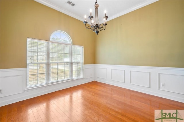 spare room featuring light wood-style floors, visible vents, a notable chandelier, and ornamental molding