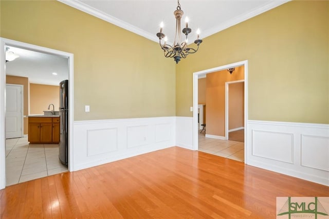 unfurnished room with a wainscoted wall, crown molding, light wood finished floors, and an inviting chandelier