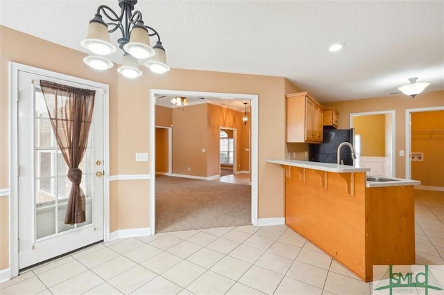 kitchen with light tile patterned floors, light countertops, freestanding refrigerator, a sink, and a peninsula