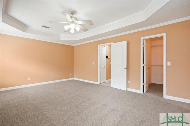 unfurnished bedroom featuring a spacious closet, a tray ceiling, carpet flooring, and visible vents