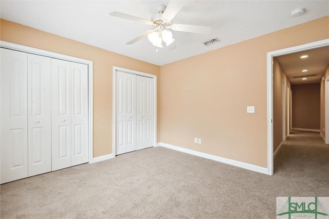 unfurnished bedroom featuring carpet floors, two closets, visible vents, and baseboards