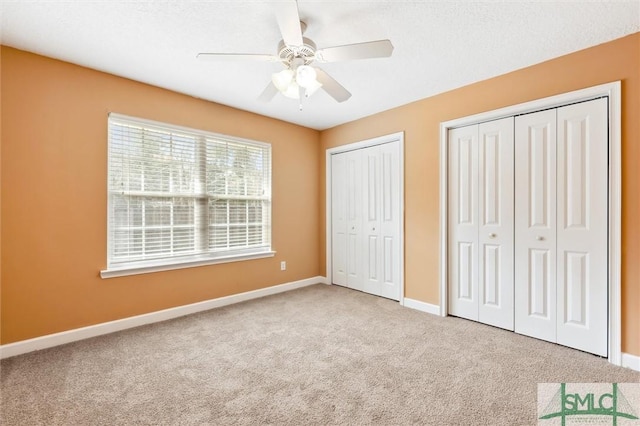 unfurnished bedroom featuring carpet flooring, ceiling fan, baseboards, and two closets