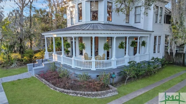 view of side of home featuring a porch, a standing seam roof, fence, and metal roof