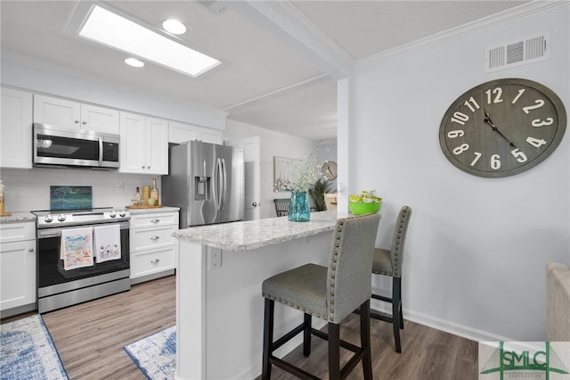 kitchen featuring stainless steel appliances, a breakfast bar, white cabinetry, visible vents, and crown molding