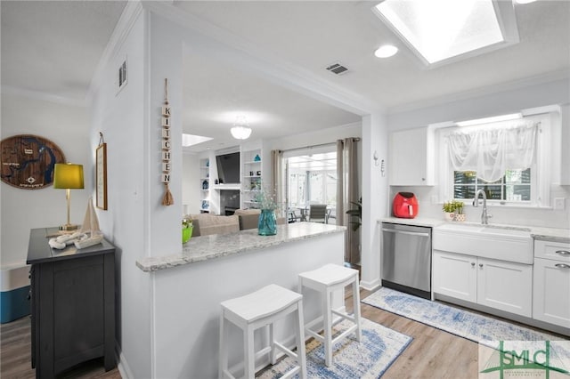 kitchen featuring light wood-style flooring, a fireplace, visible vents, dishwasher, and crown molding