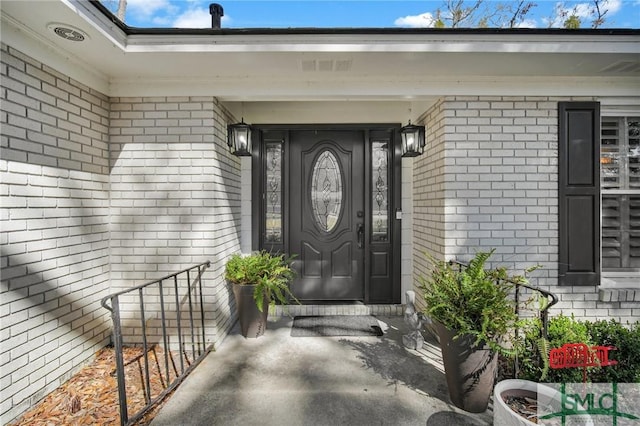 view of exterior entry featuring brick siding and visible vents