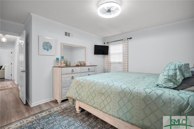 bedroom featuring baseboards, visible vents, wood finished floors, and ornamental molding