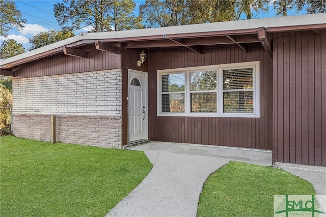 doorway to property with brick siding and a yard