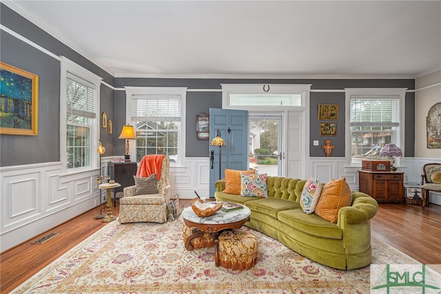 living area featuring a wainscoted wall, crown molding, visible vents, and wood finished floors