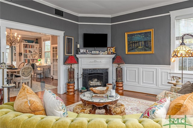 living area with a notable chandelier, a fireplace, wood finished floors, visible vents, and crown molding