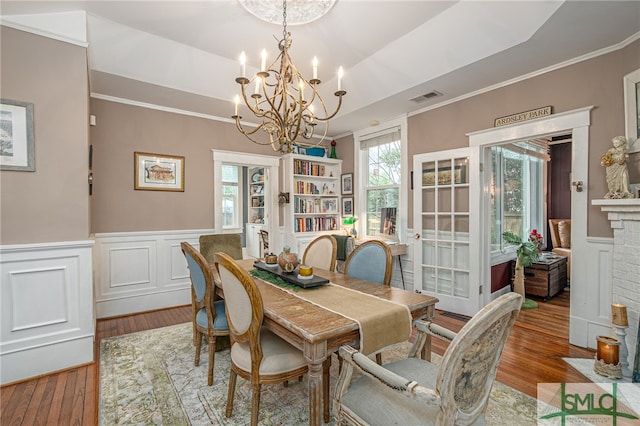 dining area with visible vents, a raised ceiling, a wainscoted wall, wood finished floors, and crown molding