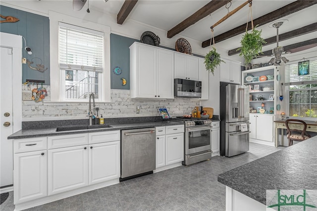 kitchen with dark countertops, appliances with stainless steel finishes, a ceiling fan, white cabinets, and a sink