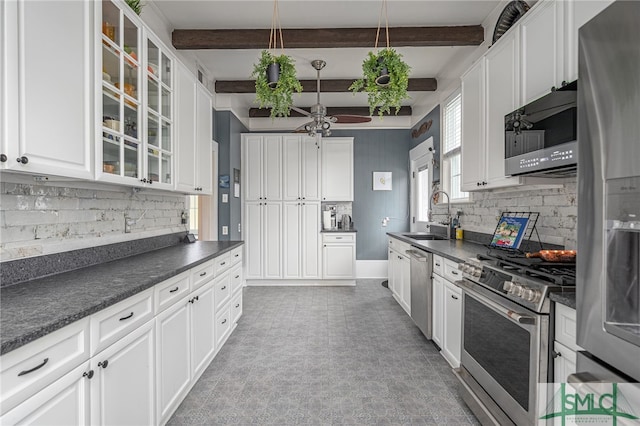 kitchen with stainless steel appliances, dark countertops, a sink, and white cabinetry