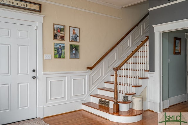 foyer entrance featuring wainscoting, wood finished floors, stairs, crown molding, and a decorative wall